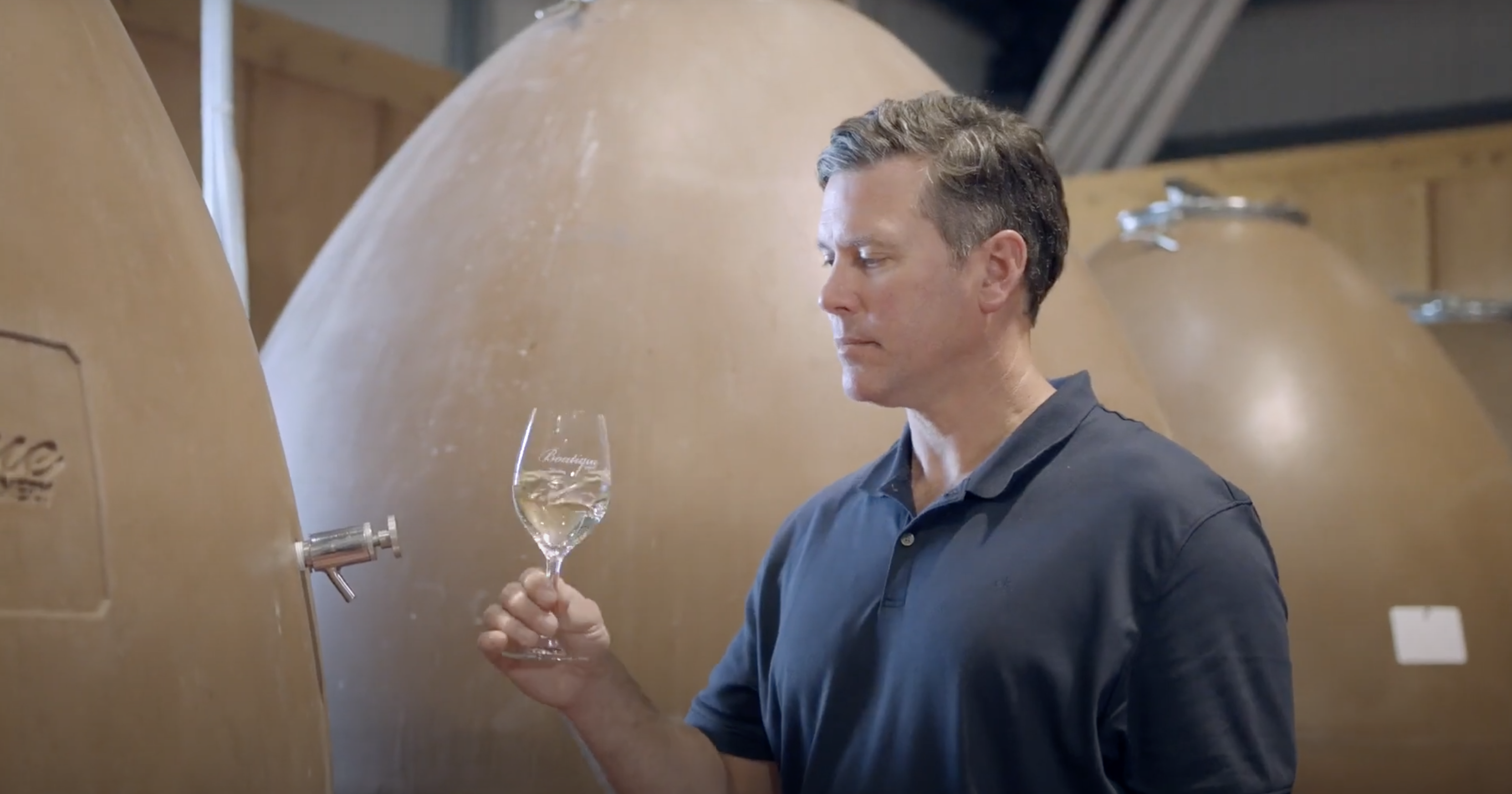 Winemaker tasting a white wine in front of concrete eggs